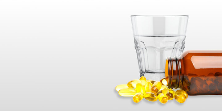 Omega 3. Fish oil capsules spill from amber bottle next to glass of water.