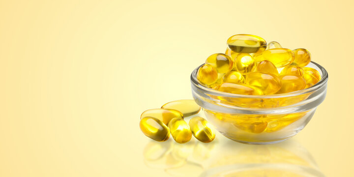 Omega 3. Fish oil capsules are neatly arranged in glass bowl showcasing their vibrant color.
