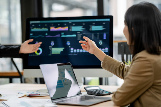 Business people discussing data visualizations on a monitor, analyzing financial charts and reports to develop a strategic plan