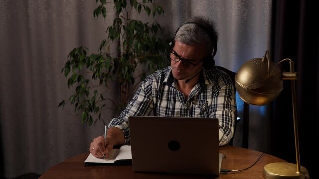 Freelancer working from home while taking notes and planning tasks at home office desk with laptop