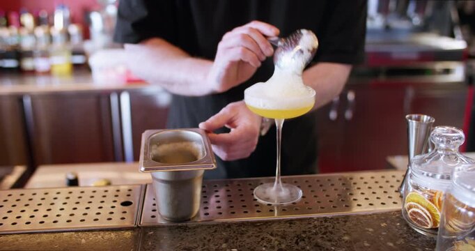 Garnishing beverage. Bartender occupation. Man hand adding white froth top with julep strainer to yellow cocktail in stemmed glass.