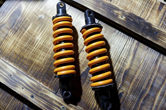Pair of worn yellow spring shock absorbers removed from an electric bike, resting on a textured wooden background, industrial garage equipment for suspension repair or maintenance project