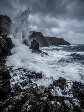 Powerful ocean waves crashing against rocky cliffs under a stormy sky.