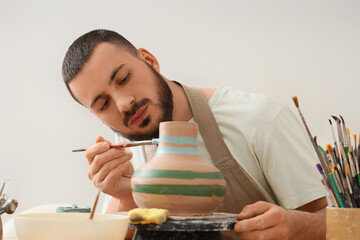 Craftsmanship and creative hobby, artisan man painting a handmade ceramic vase in a pottery studio with focus and artistic skill for home decor © Pixel-Shot