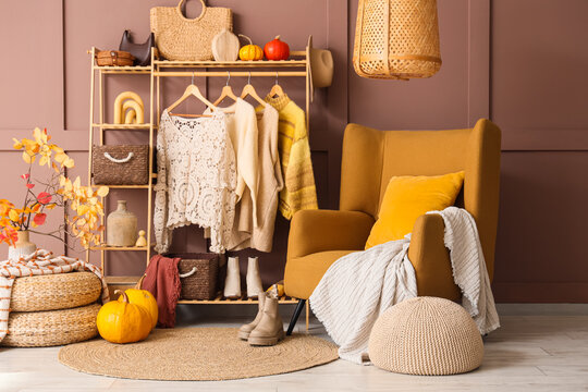 Interior of living room with comfortable armchair, poufs, autumn decor and rack with clothes