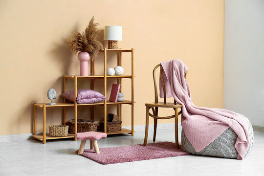 Pouf with stool, shelving unit and different coral decor near beige wall in living room