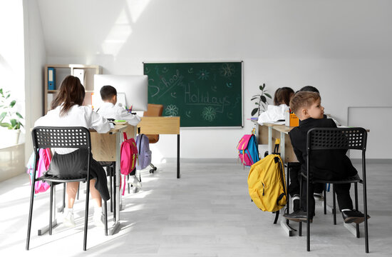 Cute little pupils sitting at desks in classroom, back view. School holidays concept