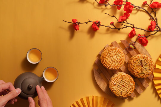 Top view of hands holding teapot next to mooncakes for Mid-Autumn Festival celebration
