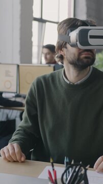 Young man office worker wearing virtual reality glasses moving head looking around at desk in workplace. Entertainment and modern technology concept.