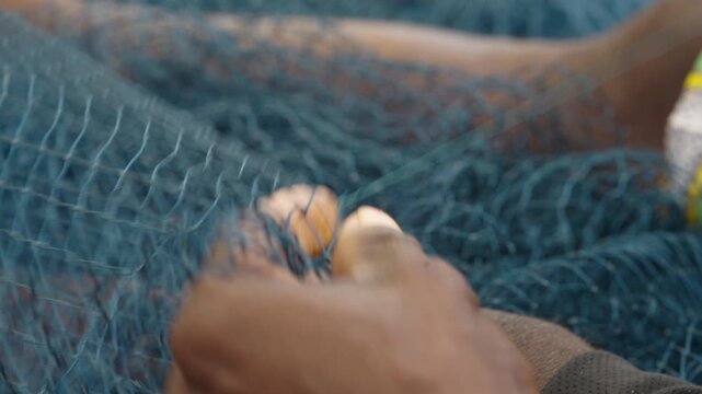 Hands repair blue fishing net with a small weaving tool in a detailed close-up of traditional work, African coastal fishing village