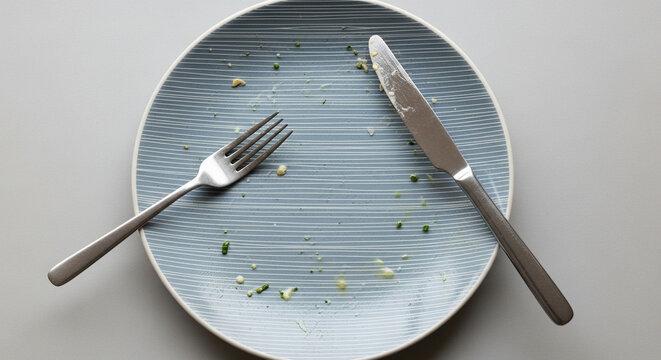 Empty plate with fork and knife after a meal on a grey background