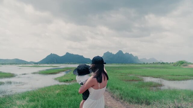 4K Asian young woman holding baby in arms standing outdoors in nature during family trip.	
