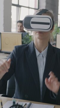 Young woman using virtual reality glasses moving hands sitting at desk in coworking office. Innovation and workplace fun concept.