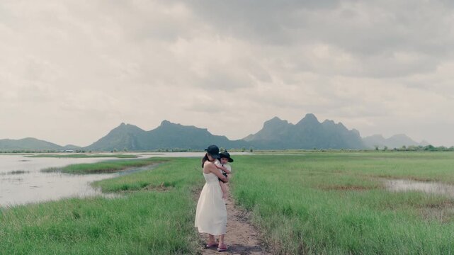 4K Asian young woman holding baby in arms standing outdoors in nature during family trip.	
