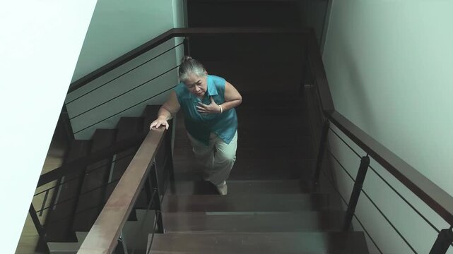 asian senior woman struggling to climb stairs due to weak body, panting and breathless while ascending at home