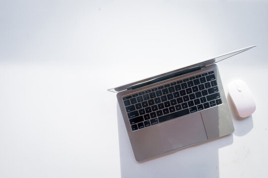 Top view of a silver laptop computer and a white wireless mouse on a bright white background with large copy space. Concept of minimalist workspace, freelance, work from home, and online business.