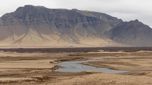 Kitesurfer rides across shallow water and sediment channels beneath Eystrahorn at Lon Lagoon, Hornafjordur, East Iceland, Iceland, Europe, drone tracking