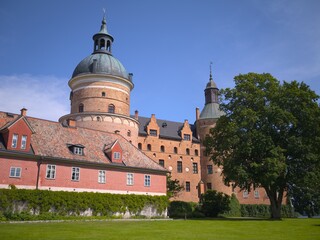 Historic red brick castle with large dome tower and green trees on sunny day © IMRAN_IM33