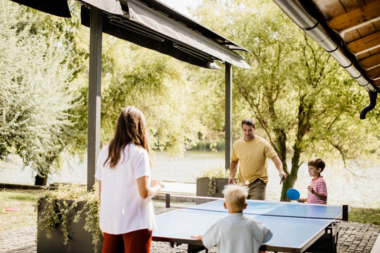 Family enjoys a lively game of ping pong beside a serene lake