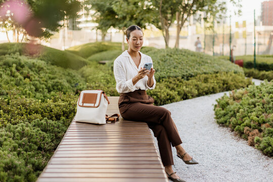 Korean woman enjoys peaceful moment in urban garden while using smartphone
