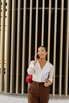 Korean woman enjoying sunlight while chatting on the phone in a modern setting
