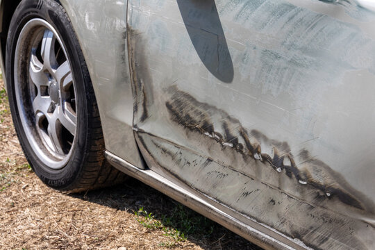 Close-up of a damaged silver car door with deep scratches and dent after a traffic accident, photographed outdoors in bright daylight for auto insurance concept. car crash