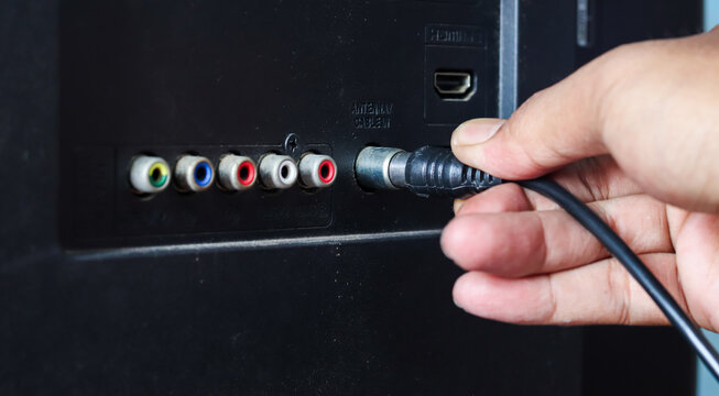 Asian man connecting an antenna cable to a television at home. Close-up of plugging in a TV antenna cable for broadcast signal reception and home entertainment.