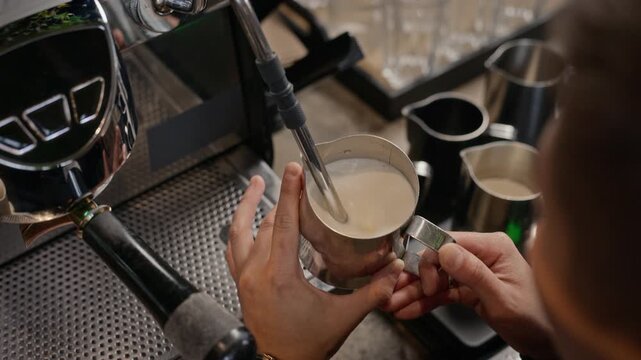 Barista steaming milk in metal pitcher using espresso machine steam wand. Clip serves cafe advertising, barista training tutorials, and beverage marketing campaigns