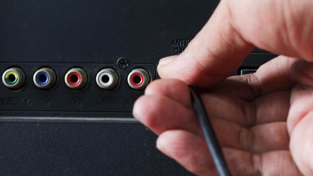 Asian man connecting an antenna cable to a television at home. Close-up of plugging in a TV antenna cable for broadcast signal reception and home entertainment.