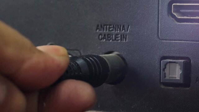 Asian man connecting an antenna cable to a television at home. Close-up of plugging in a TV antenna cable for broadcast signal reception and home entertainment.
