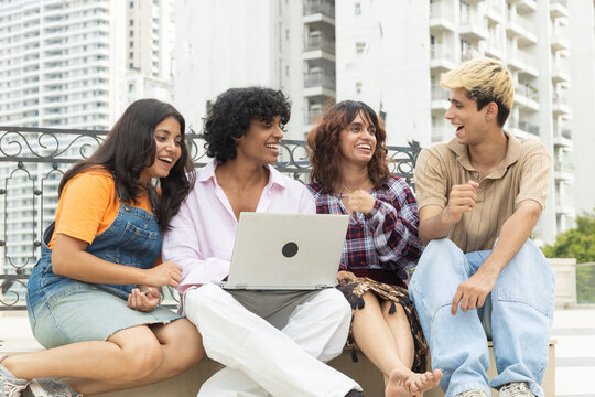Group of young diverse indian asian students sitting outdoors. engaging in lively discussion while working together on laptop. collaboration and friendship in modern education in india