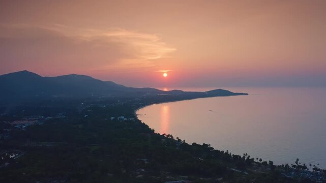 Koh Samui tropical island vibrant sunset over a tranquil bay, showcasing the curving coastline with lush green hills meeting the calm ocean waters reflecting the colorful sky. Panoramic aerial view