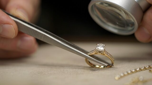 A jeweler inspects a diamond ring with tweezers and a magnifying glass. Perfect for luxury retail and fine jewelry craftsmanship marketing concepts.