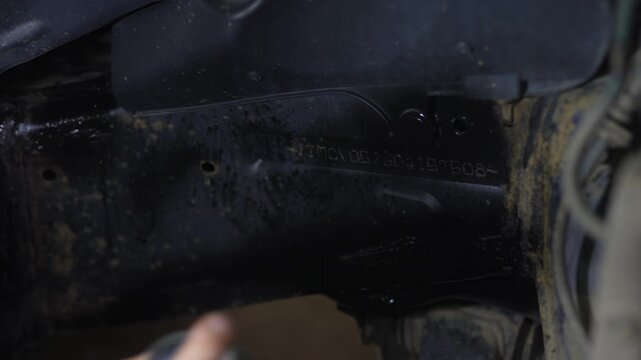 Man spraying black protective anti-corrosion coating onto car chassis part.