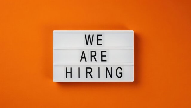 A light box with We Are Hiring sign against a vibrant orange background. Perfect for corporate recruitment campaigns and modern job advertisement concepts.