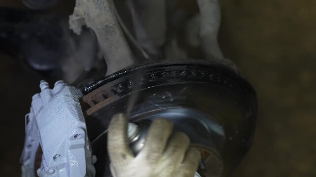 Man spraying aerosol cleaner onto a car ventilated brake rotor.