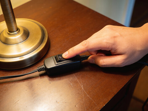 Close-Up of Hand Pressing Accessible Rocker Switch on Warm Home Table Lamp