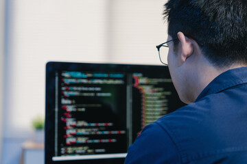 Young programmer coding software on computer screen at workplace
