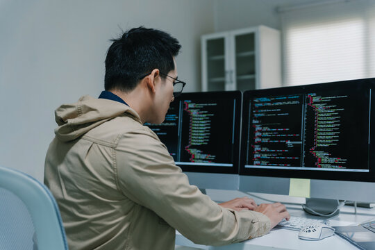 Programmer coding software on multiple computer monitors at workstation