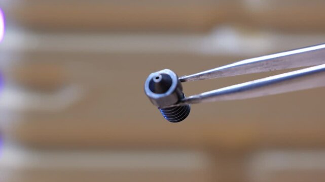 Extreme close-up of metal tweezers holding a large 1mm nozzle for a 3D printer hotend extruder