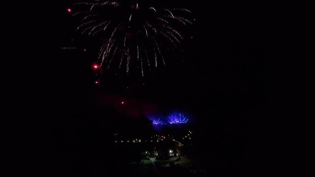 Stunning aerial footage captures vivid fireworks exploding over glowing buildings at night, with vibrant colors lighting up the dark skyline. Crisp, wide angle drone video, perfect for celebrations.