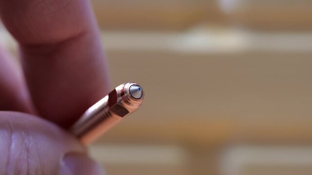 Close-up of male fingers holding and inspecting a hardened steel tipped copper nozzle for a 3D printer hotend