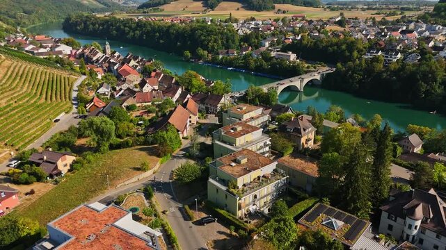 Aerial view of Eglisau, Switzerland, with vineyards and historic homes along the turquoise Rhine, crossed by an arched bridge amid green hills and countryside.