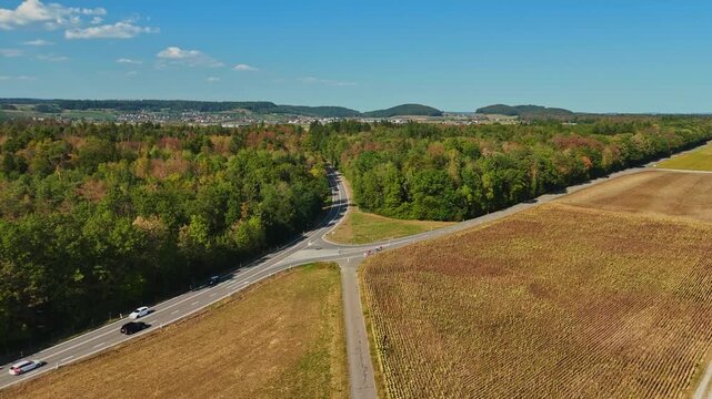 Aerial view near Eglisau, Switzerland, showing a rural road junction between dense woodland and agricultural fields, with a passing car and rolling countryside under clear summer skies.