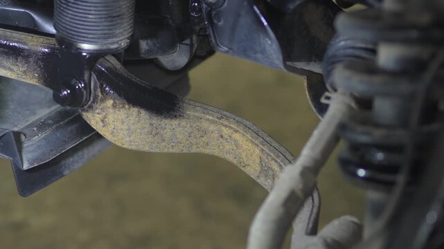 Man spraying black protective anti-corrosion coating onto car chassis part.