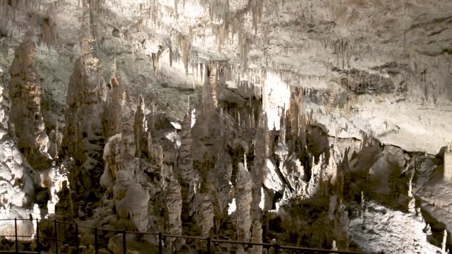 Stunning underground stalagmites and stalactites formations illuminated in postojna cave, slovenia, showcasing natural rock sculptures and an ancient pathway.