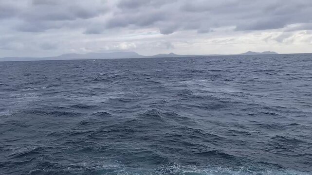 Motion footage of choppy dark blue ocean waves with distant land under clouds