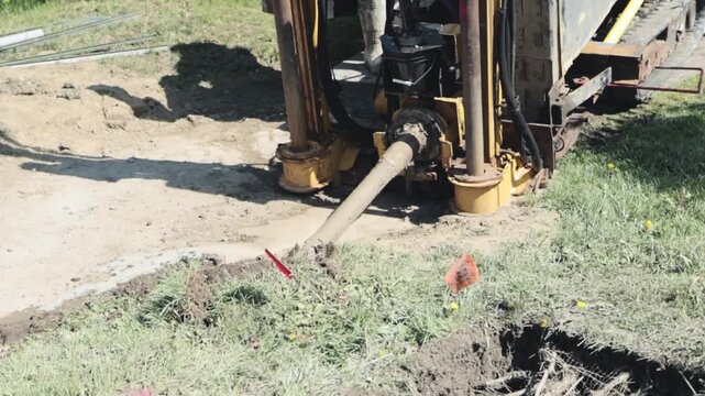 A directional drilling machine drives a drill bit underground from a grassy work area toward a small excavation for street lighting electrical conduit installation.