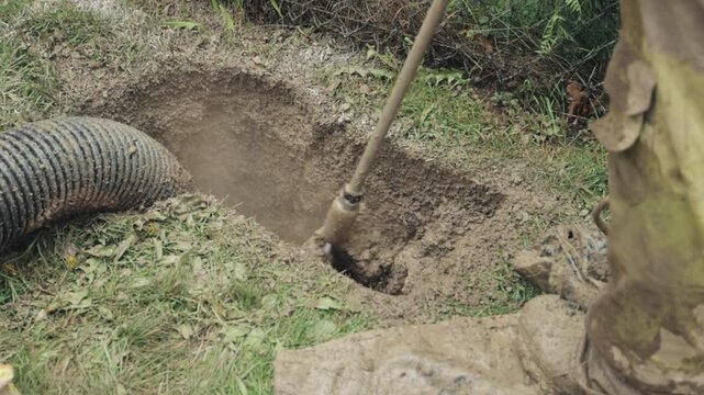 Hydrovac excavation exposes a pole hole on a grassy verge while crews prepare the site for street lighting pole foundation and conduit work; vacuum hose and soil slurry are visible, emphasizing safe u