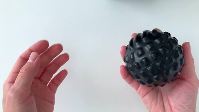 Close-up. A woman throws a black massage ball from palm to palm, doing hand exercises to relax muscles, relieve tension and spasm